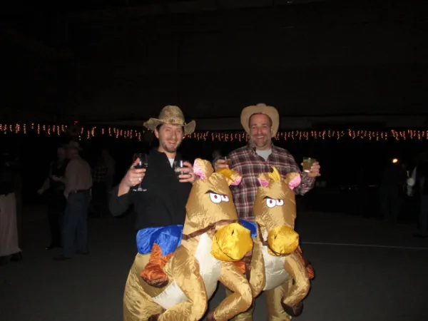 Two CWN members in cowboy hats riding an inflatable horse costume at a charity fundraiser