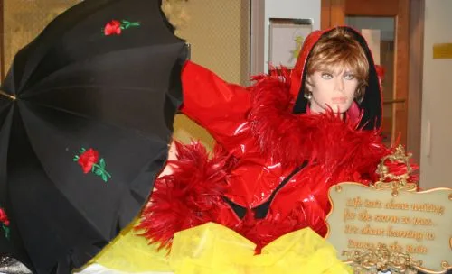 A mannequin in a red feathered outfit with a black umbrella, decorating a Dancing in the Rain themed event