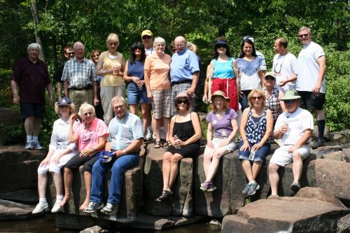 A large, smiling group of CWN members gathered on rocks in a sunny park